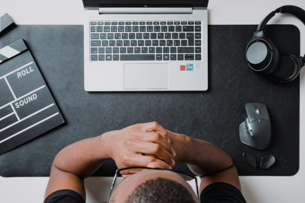 A man sits at a desk with a laptop, mouse, headphones and a clapper board, ready to create social media content.